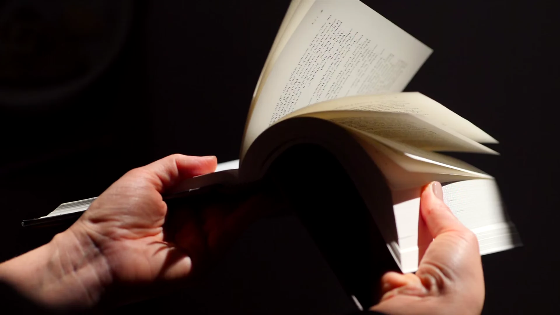 Hände blättern eine Seite in einem Hardcover-Buch um, fadengehefteter Buchblock, kühles Licht